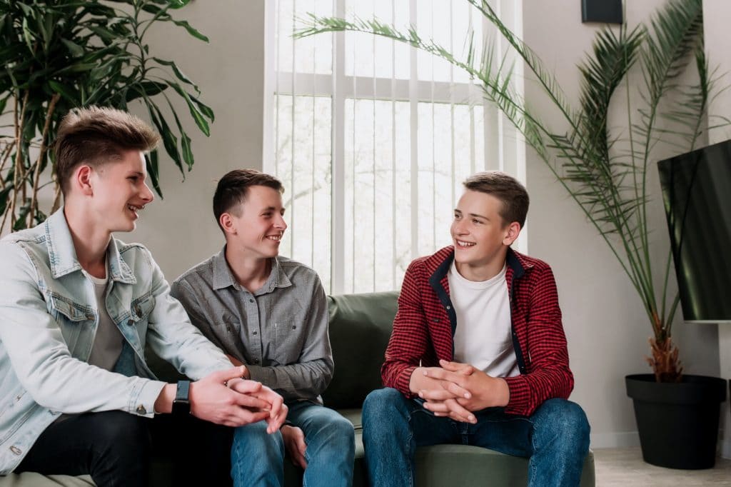 Three friends talking at green sofa in living room. Guys having a talk, gossip