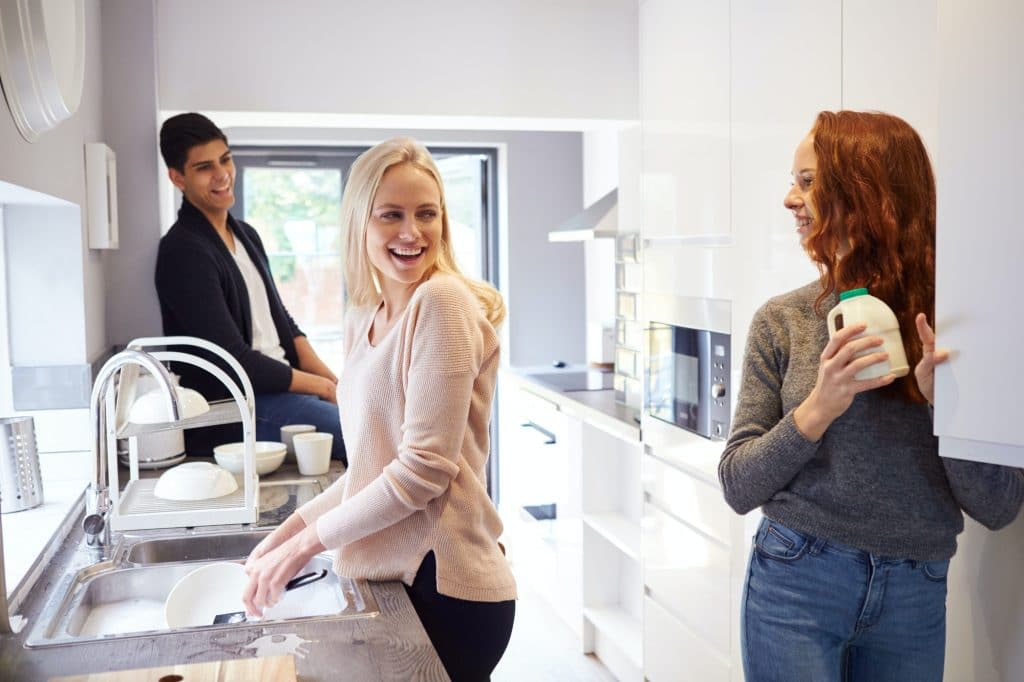 Group Of College Student Friends In Shared House Kitchen Washing Up And Hanging Out Together